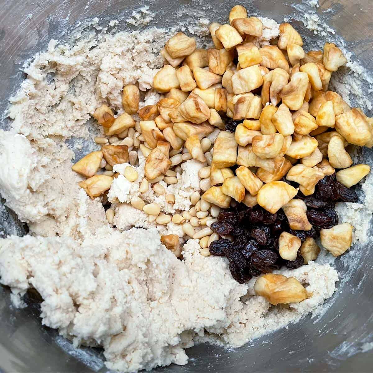 Adding raisins, pine nuts, and infused apples into a bowl of the cookie dough.