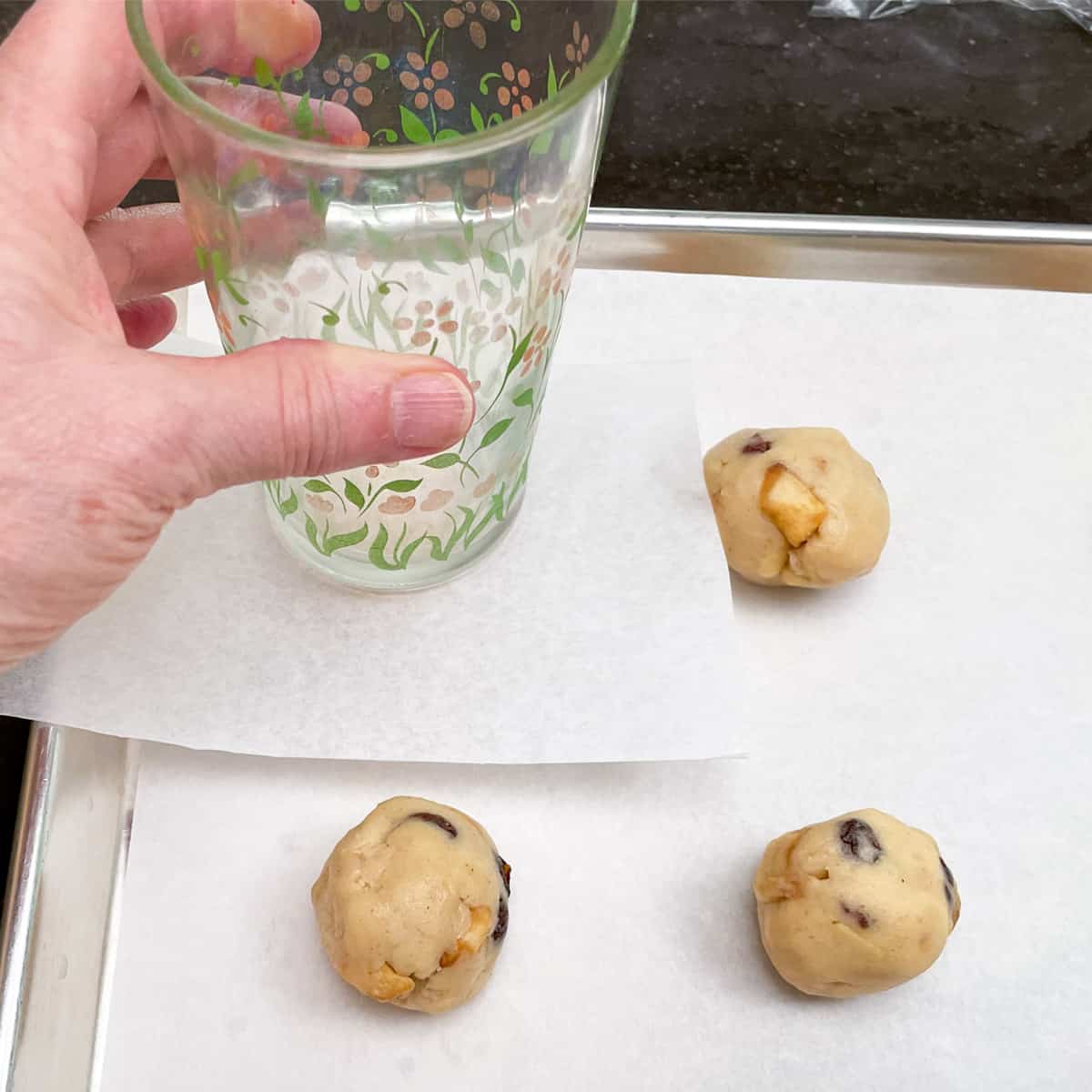 Using a parchment paper small square between the cookie ball and a flat bottom glass. To flatten the cookie ball.