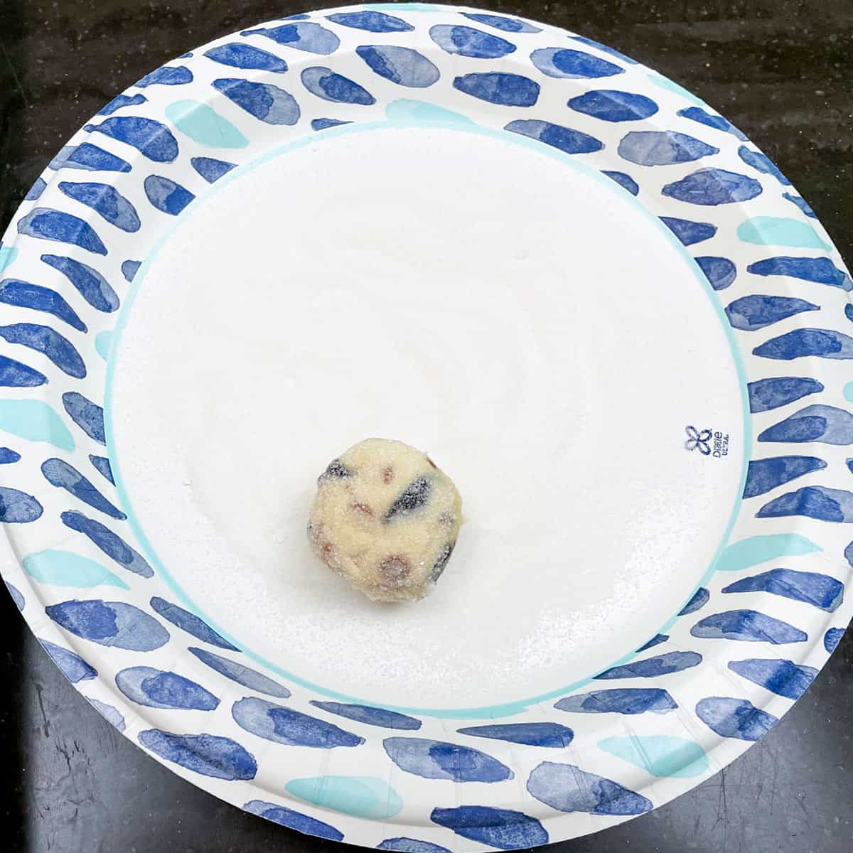 Plate of super fine sugar with a cookie ball being rolled around to coat. 