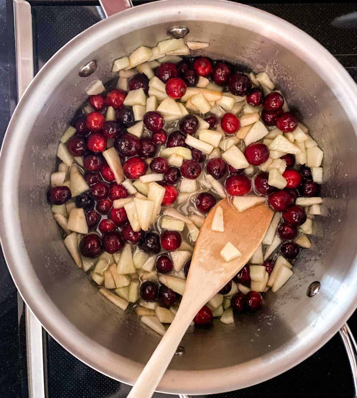 Adding whole cranberries and diced apples into a saucepan.