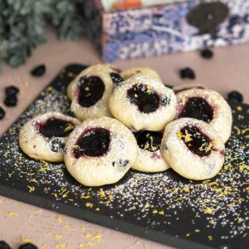 Blueberry with blueberry jam cookies on a black square serving plate with powdered sugar on top.