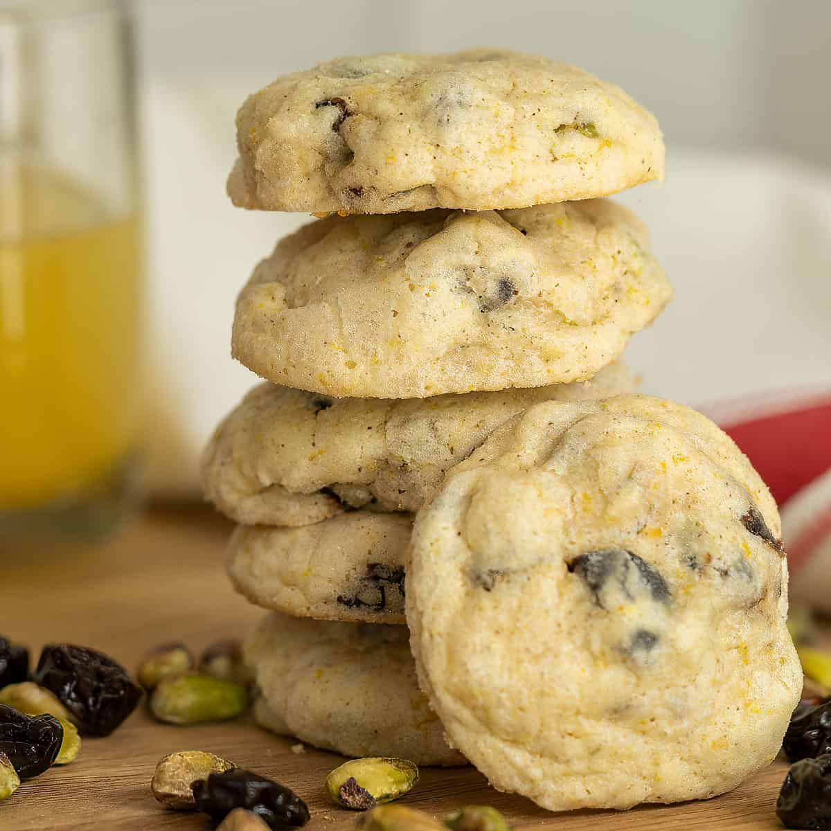 A stack of Cherries Orange pistachios cookie on a wooden cutting board with nuts, cherries around the base.