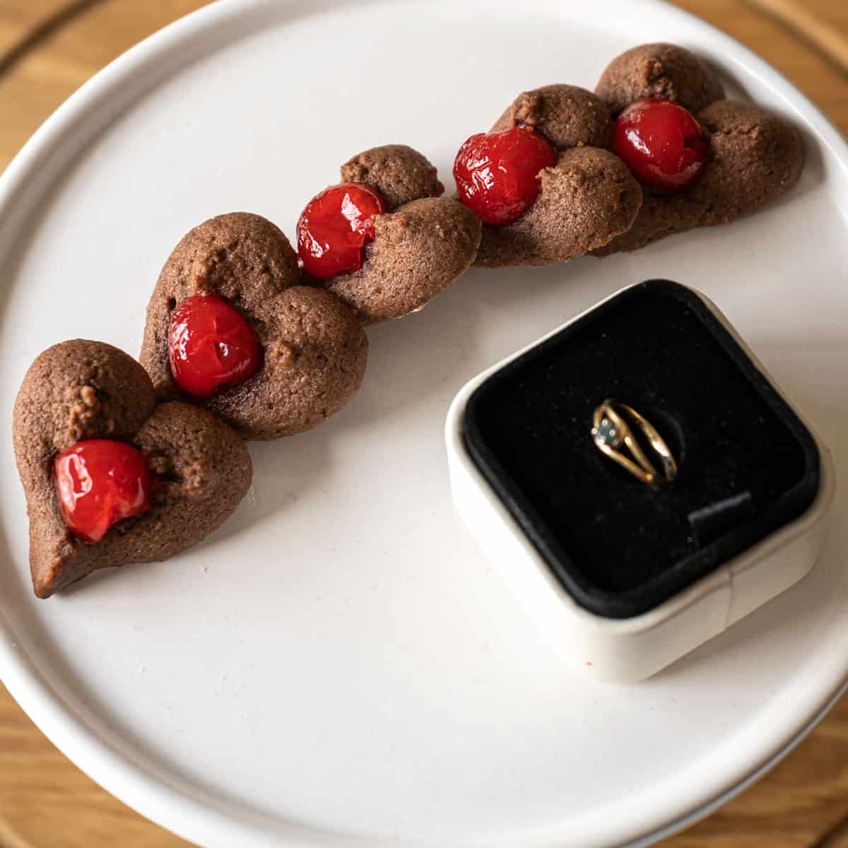 Chocolate spritz heart-shaped cookies with cherries on a white plate with a ring for Valentine's Day.