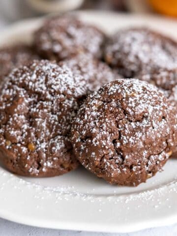 Chocolate Cookies with Orange and Toffee Bits with powdered sugar on top sitting on a white plate.