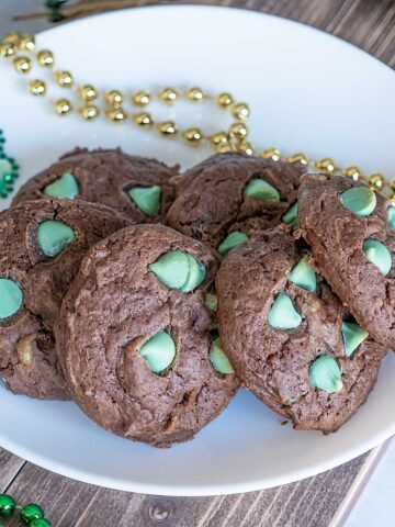 Chocolate mint cream cheese cookies sitting on a white plate with gold and green bead for decoration.