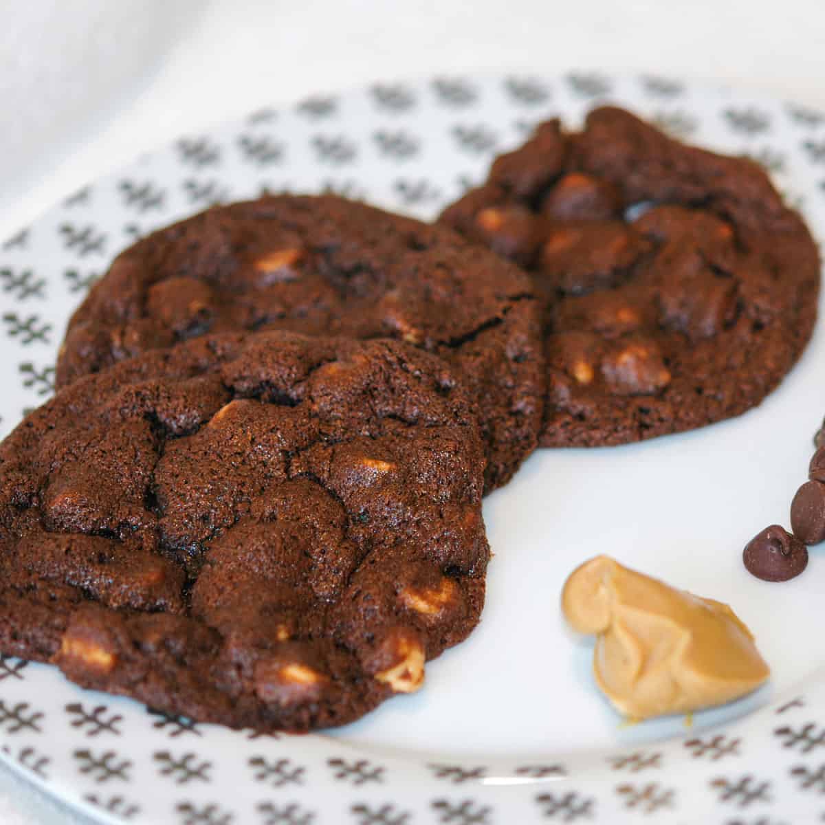 Chocolate Peanut Butter Chip cookies on a white plate with a scoop of peanut butter and a few chocolate chips.