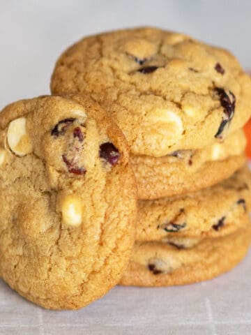 Stack of cranberry and white chocolate round cookies on a piece of parchment paper.