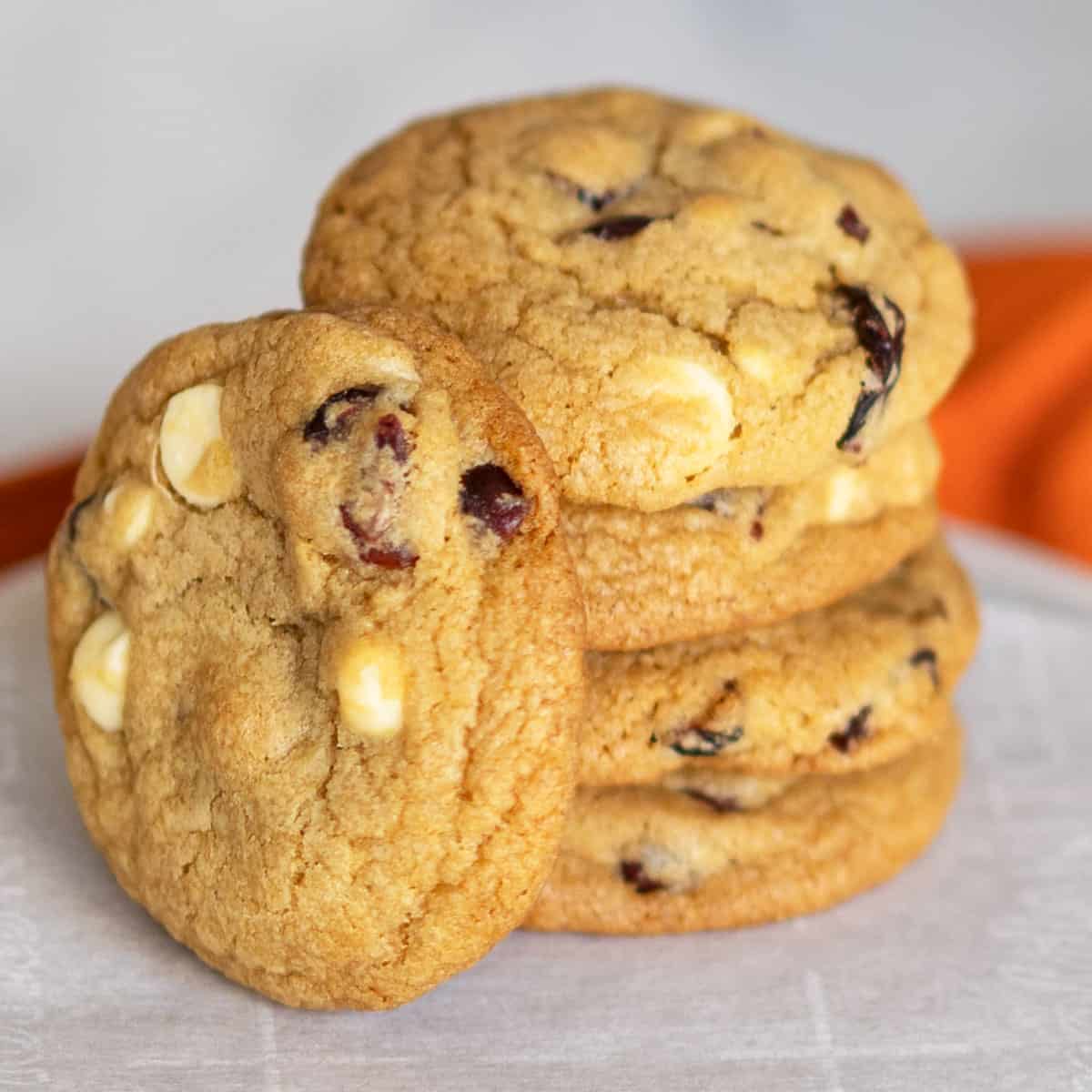 Stack of cranberry and white chocolate round cookies on a piece of parchment paper.