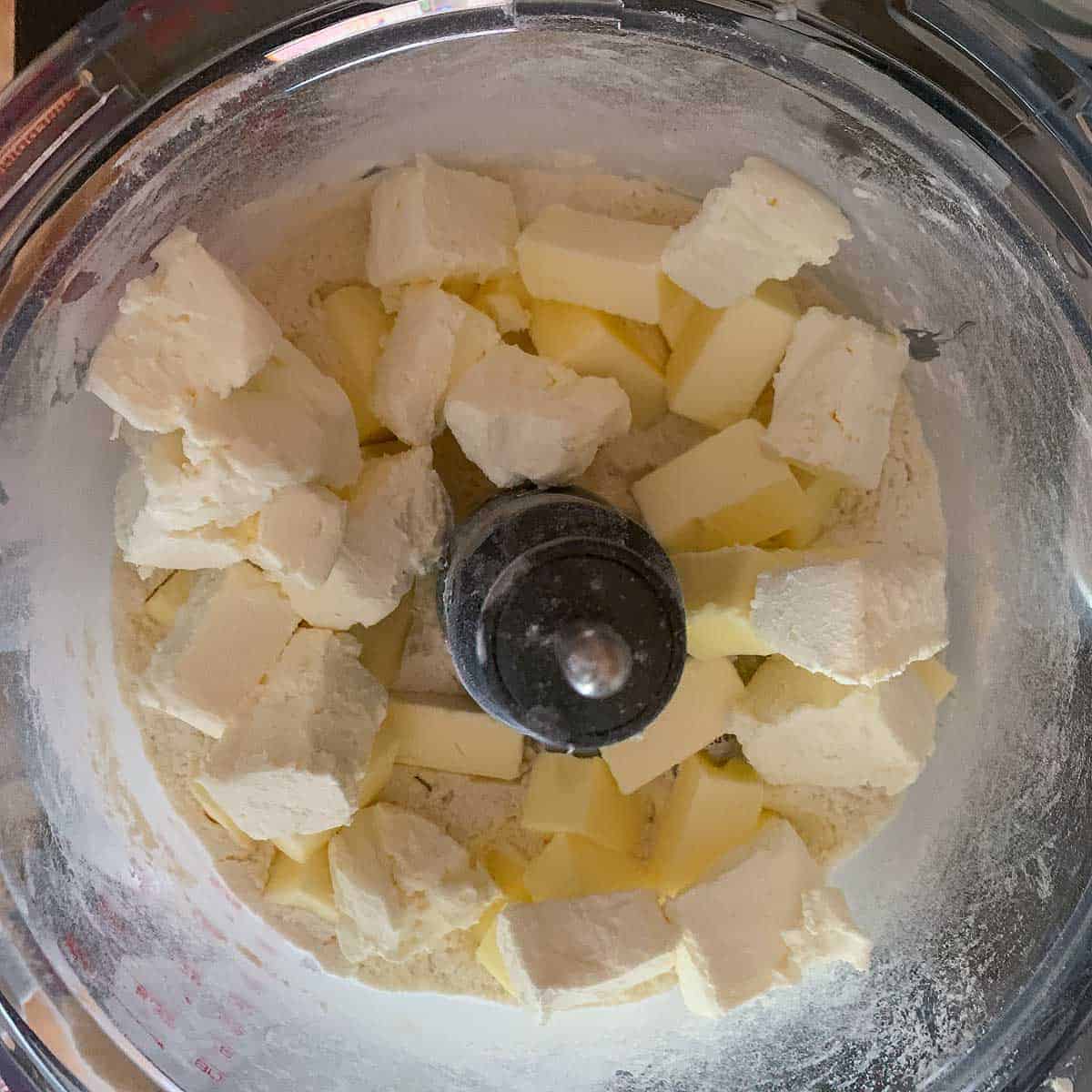 Cut up pieces of cream cheese, butter, and flour mixture in a food processor ready to mix.