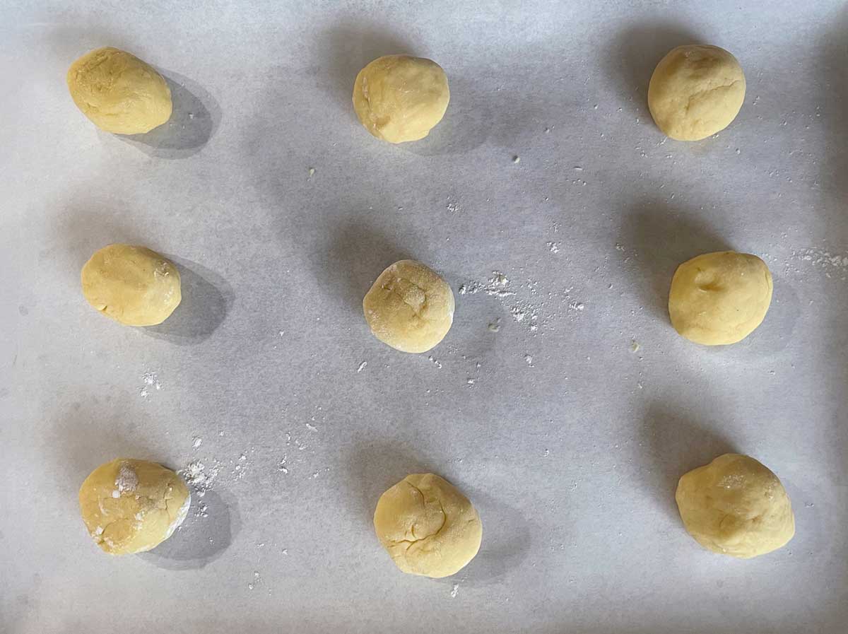 Nine balls of Italian Anise cookie dough on a parchment-lined cookie sheet pan, ready for the oven.