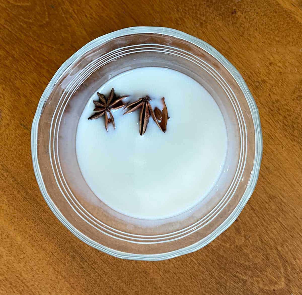 A bowl of milk that has 3 anise stars in it to give it flavor.