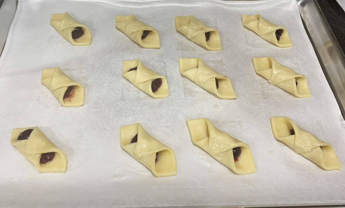 12 filled and sealed red raspberry kolache ready for the oven.