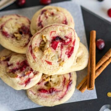 Apple Cranberry Walnut Swirl Cookies stacked with 2 cinnamon sticks on a piece of parchment paper square.