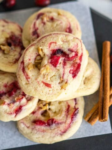 Apple Cranberry Walnut Swirl Cookies stacked with 2 cinnamon sticks on a piece of parchment paper square.