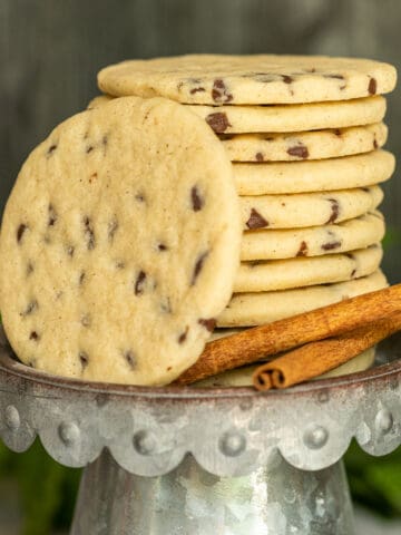Chocolate Chip Sugar cookies stacked on a metal dish with two sticks of cinnamon on the side.