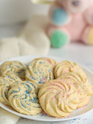 Pink and blue sparkling sugar top these round rosette style cookies on a white serving plate.