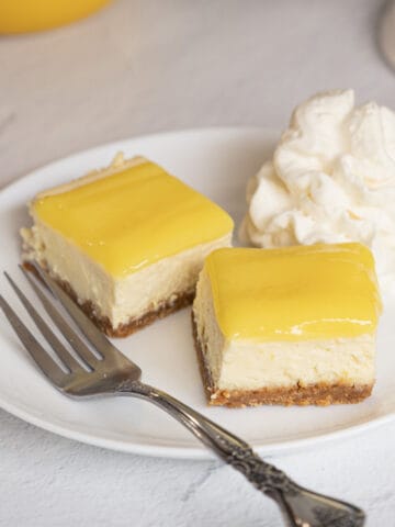 Two pieces of lemon cheesecake with lemon curd with fork and on white plate.