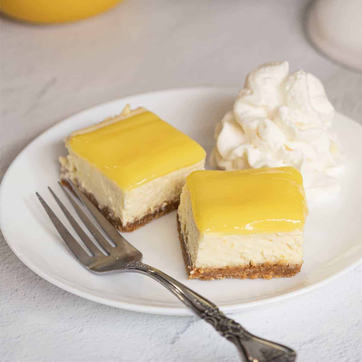 Two pieces of lemon cheesecake with lemon curd with fork and on white plate.