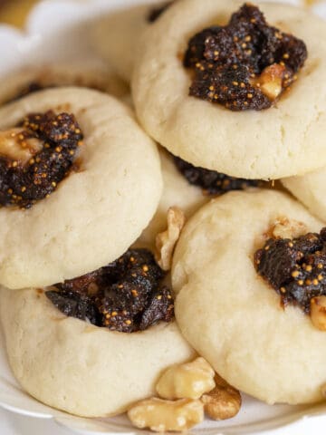 Orange Fig Thumbprint Cookies on a white dish with walnut pieces laying between the cookies.
