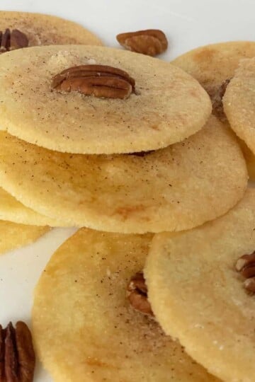 Stacks of PA Dutch Sand Tarts which are round with cinnamon sugar and a pecan half on top.
