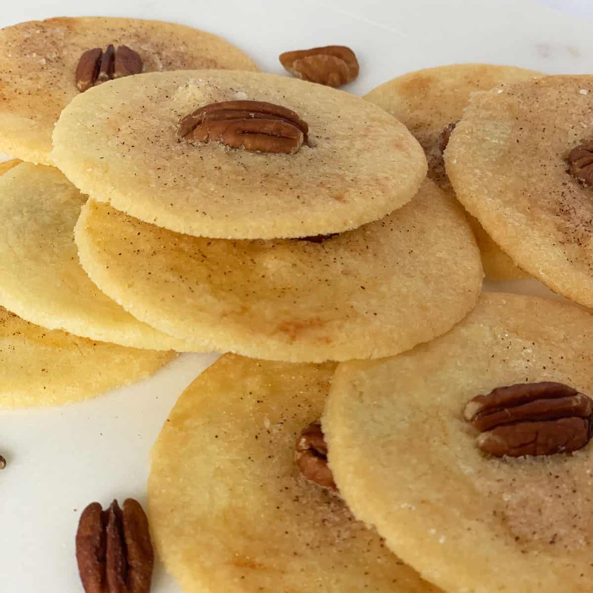 Stacks of PA Dutch Sand Tarts which are round with cinnamon sugar and a pecan half on top.