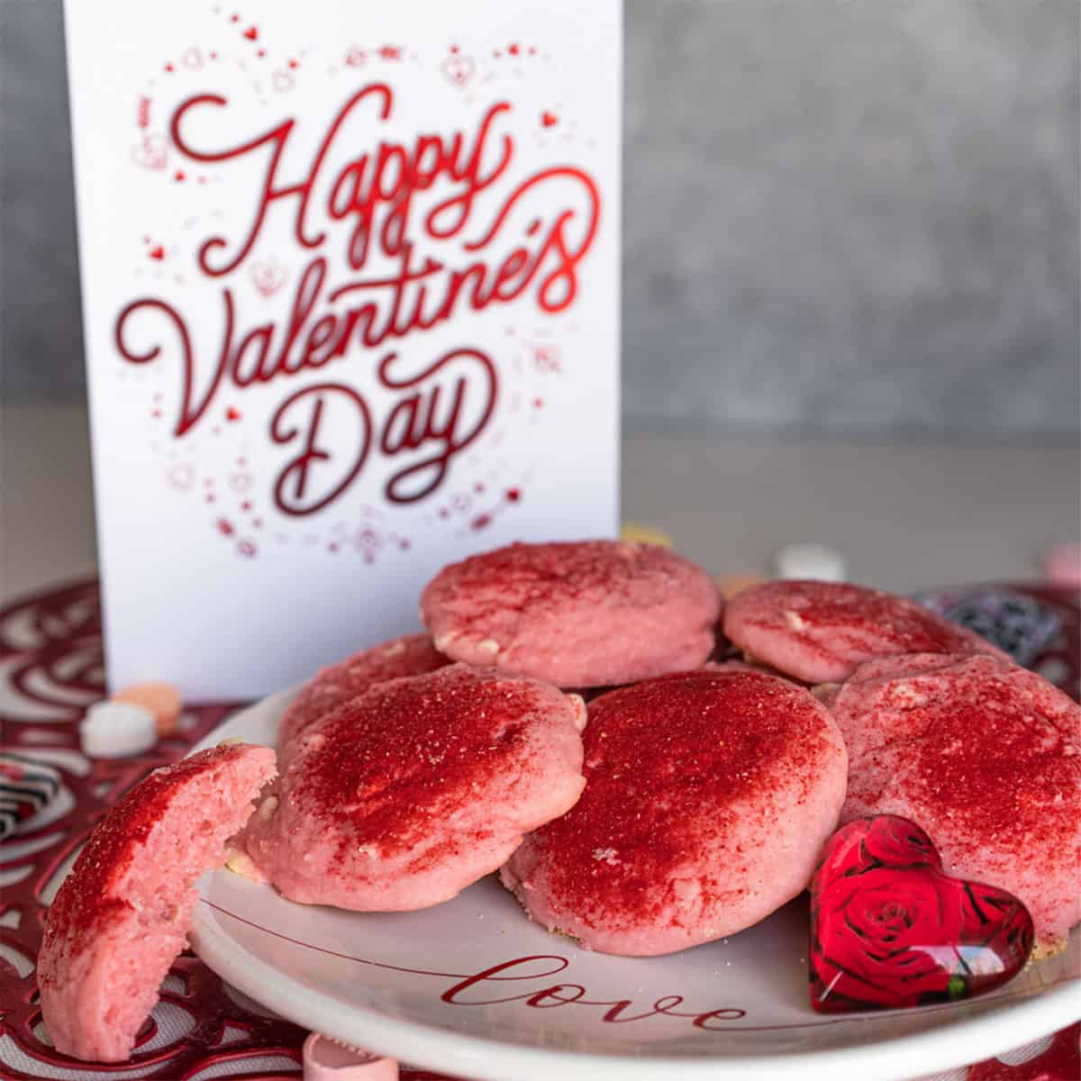 A pink and red strawberry and cream with white chocolate Valentine's Day Cookie on a white plate.