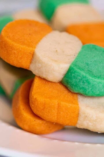 Irish-colored flag shortbread cookies on a white plate. Cookies are orange, white, and green.