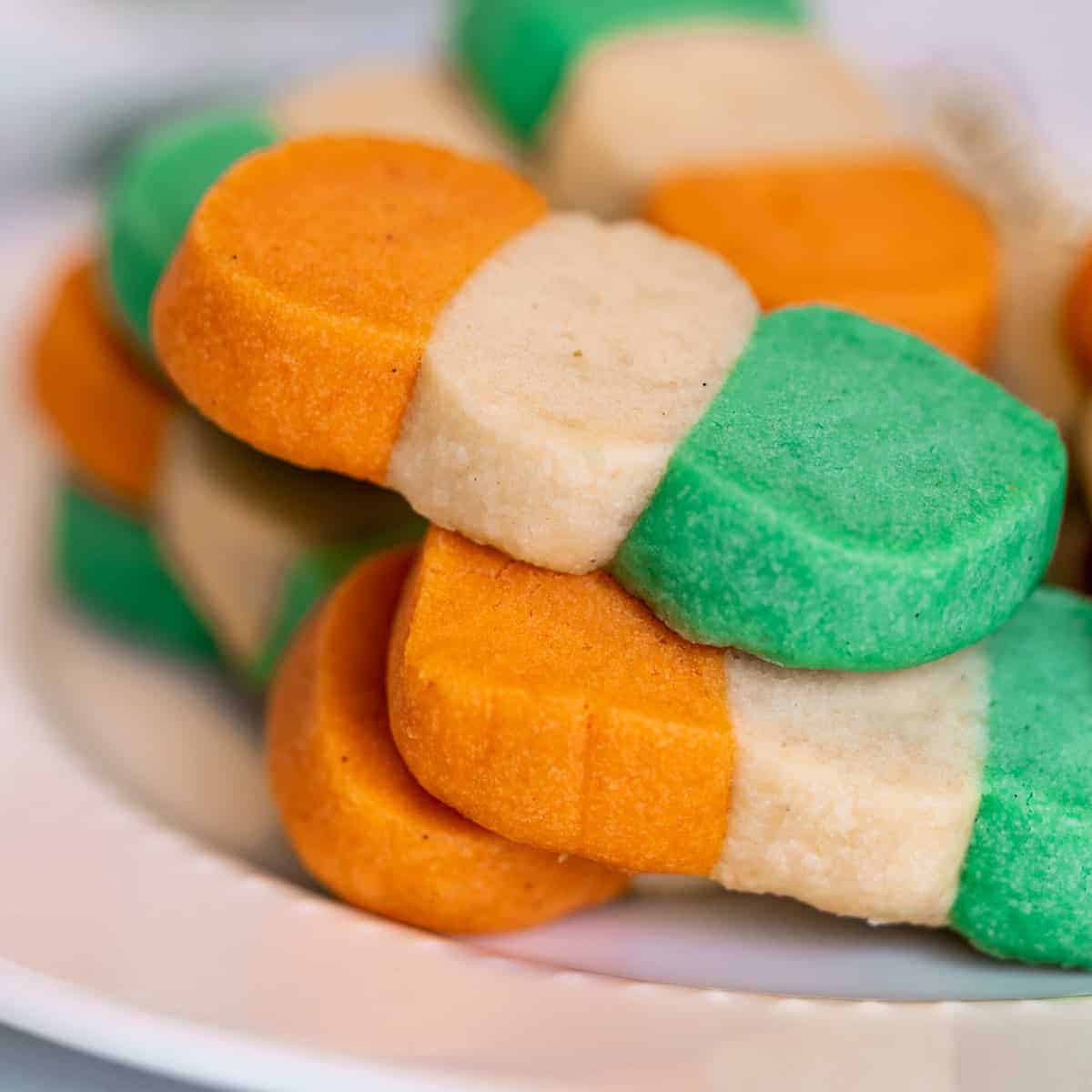 Irish-colored flag shortbread cookies on a white plate. Cookies are orange, white, and green.