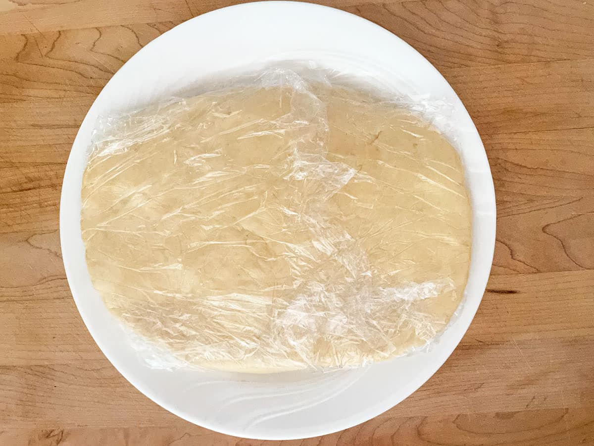 Flat oval cookie dough wrapped in plastic wrap.