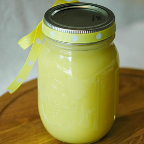 A mason style jar with homemade lemon curd in it with a yellow ribbon around the lid.