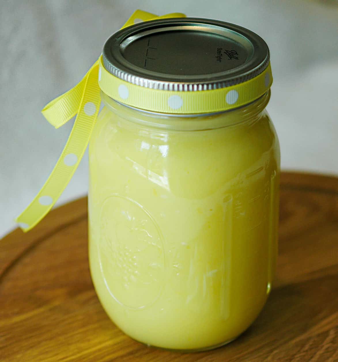 A mason style jar with homemade lemon curd in it with a yellow ribbon around the lid.