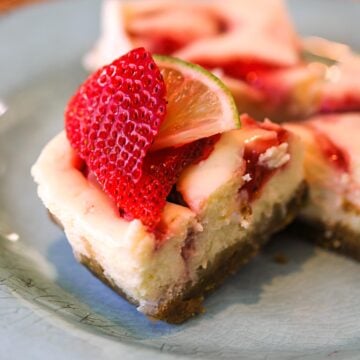 A piece of Strawberry Key Lime Cheesecake with a fresh piece of strawberry and key lime on top.