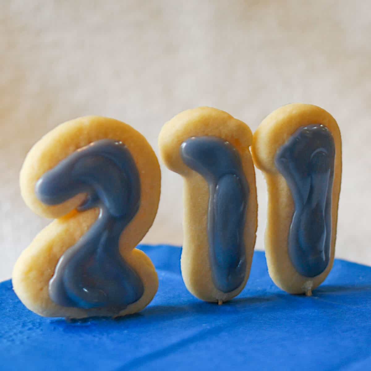 Cookies in the shape of 211 for the National 211 Day with blue icing which is their color and sitting on a blue platform.