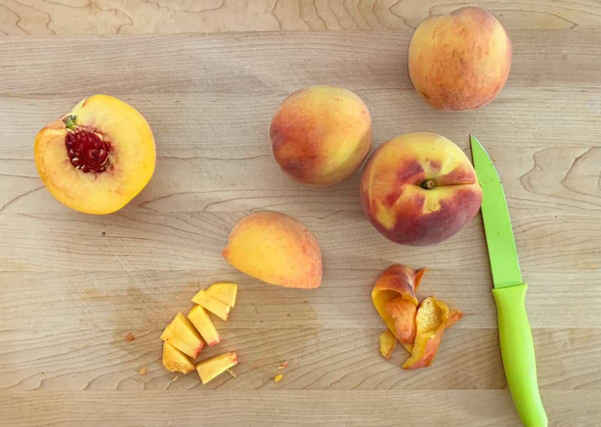 Cutting up peaches into small pieces on a cutting board.