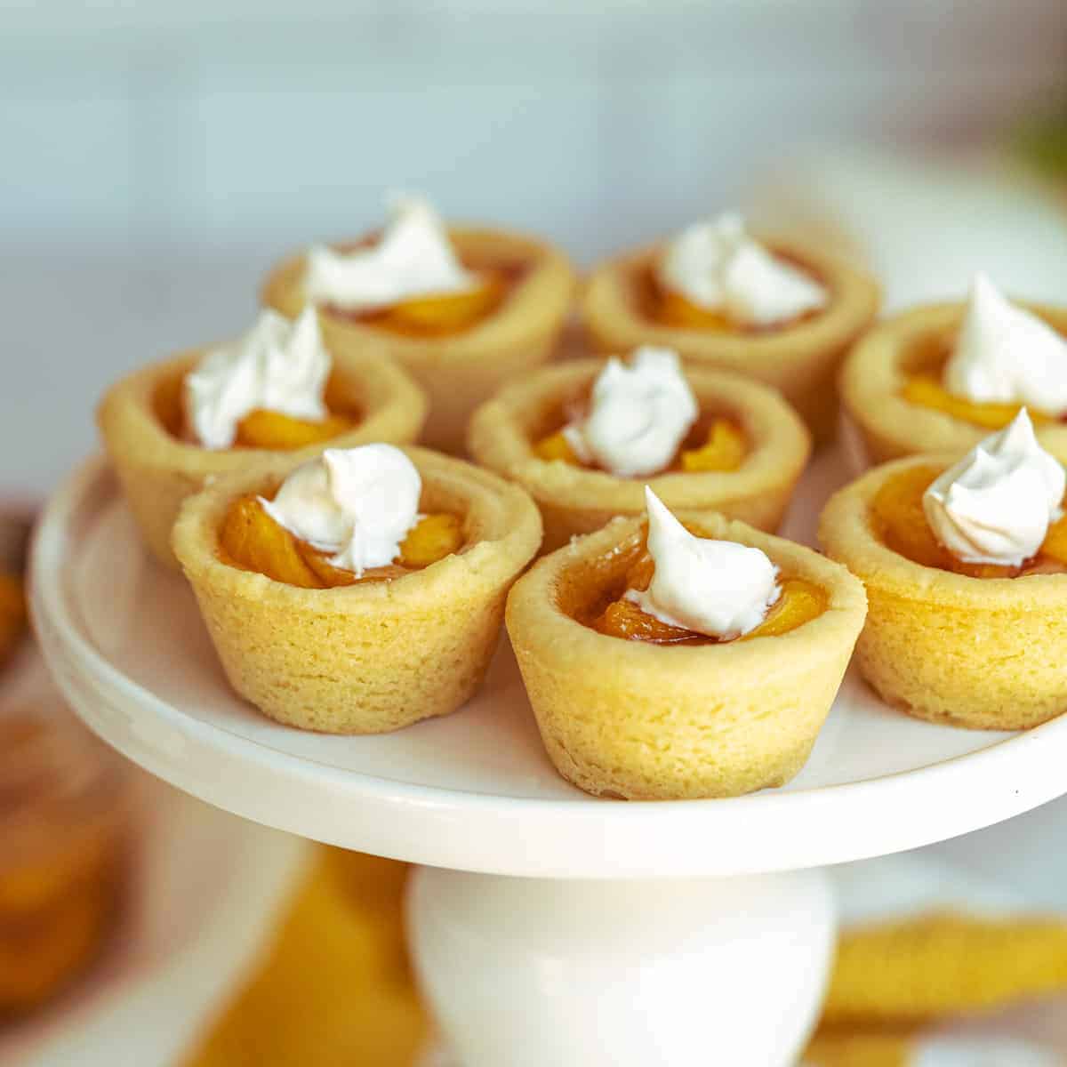 Peach Pie Cookie Cups with a dab of whip cream on top on a round pedestal serving dish.