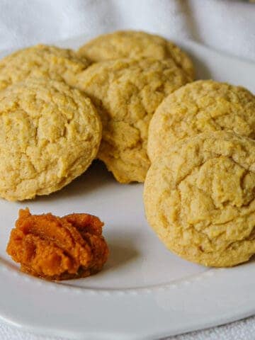 Finished Pumpkin sugar cookies on a white dish with a spoonful of pumpkin puree on the side.