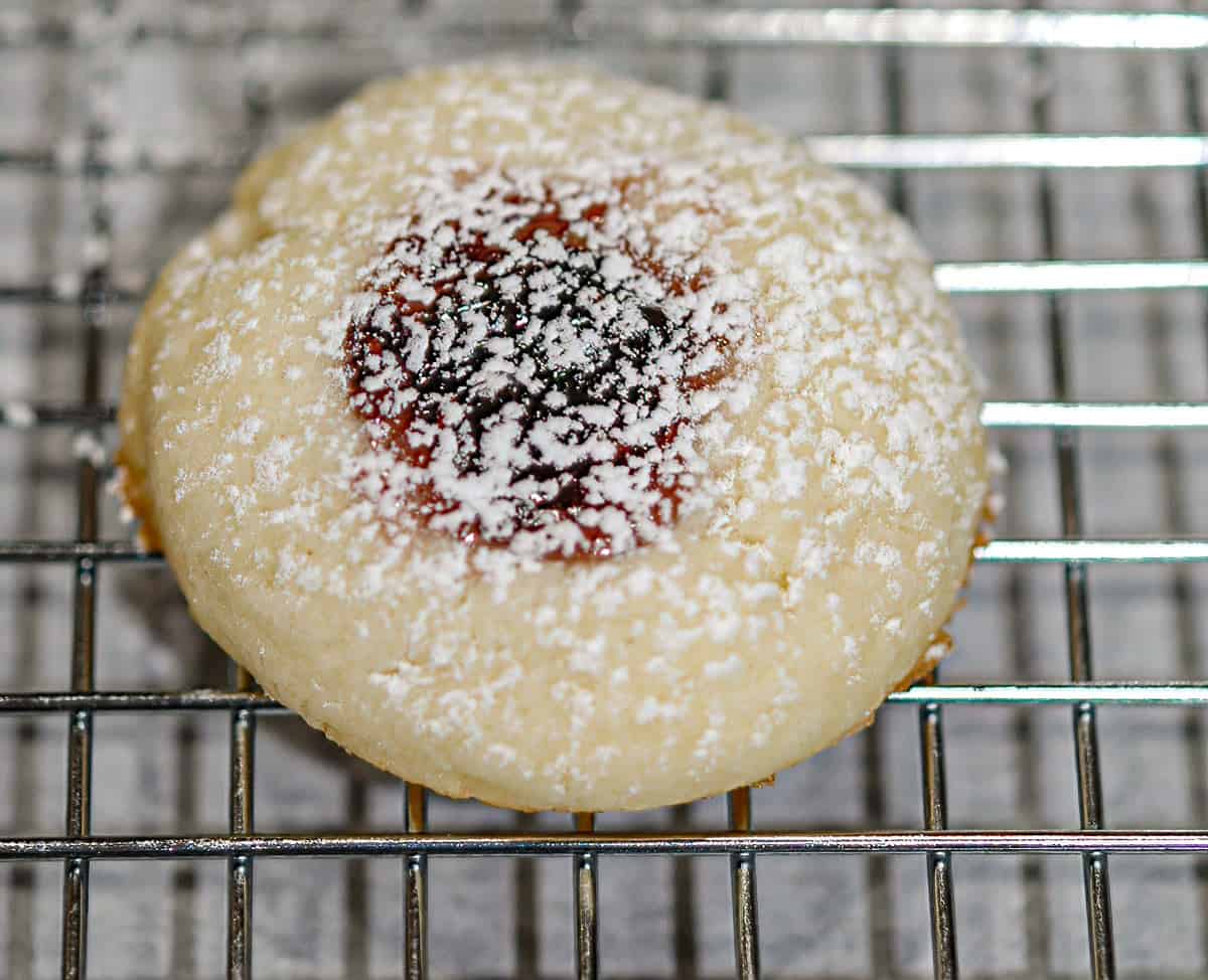 Raspberry thumbprint cookie with powdered sugar on top sitting on a cooling rack.