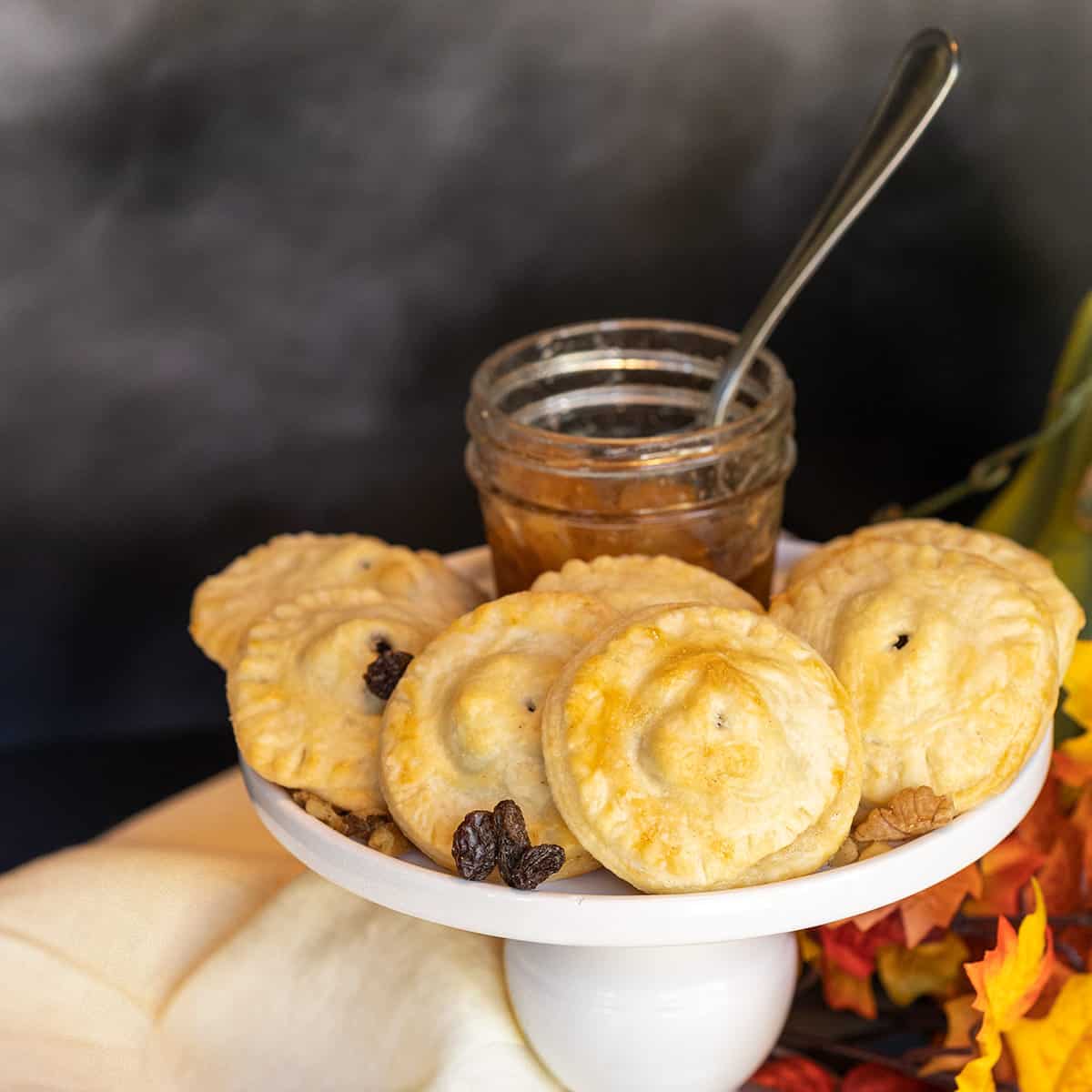 Finished apple pie cookies on a white serving plate with walnuts and raisins scattered around.