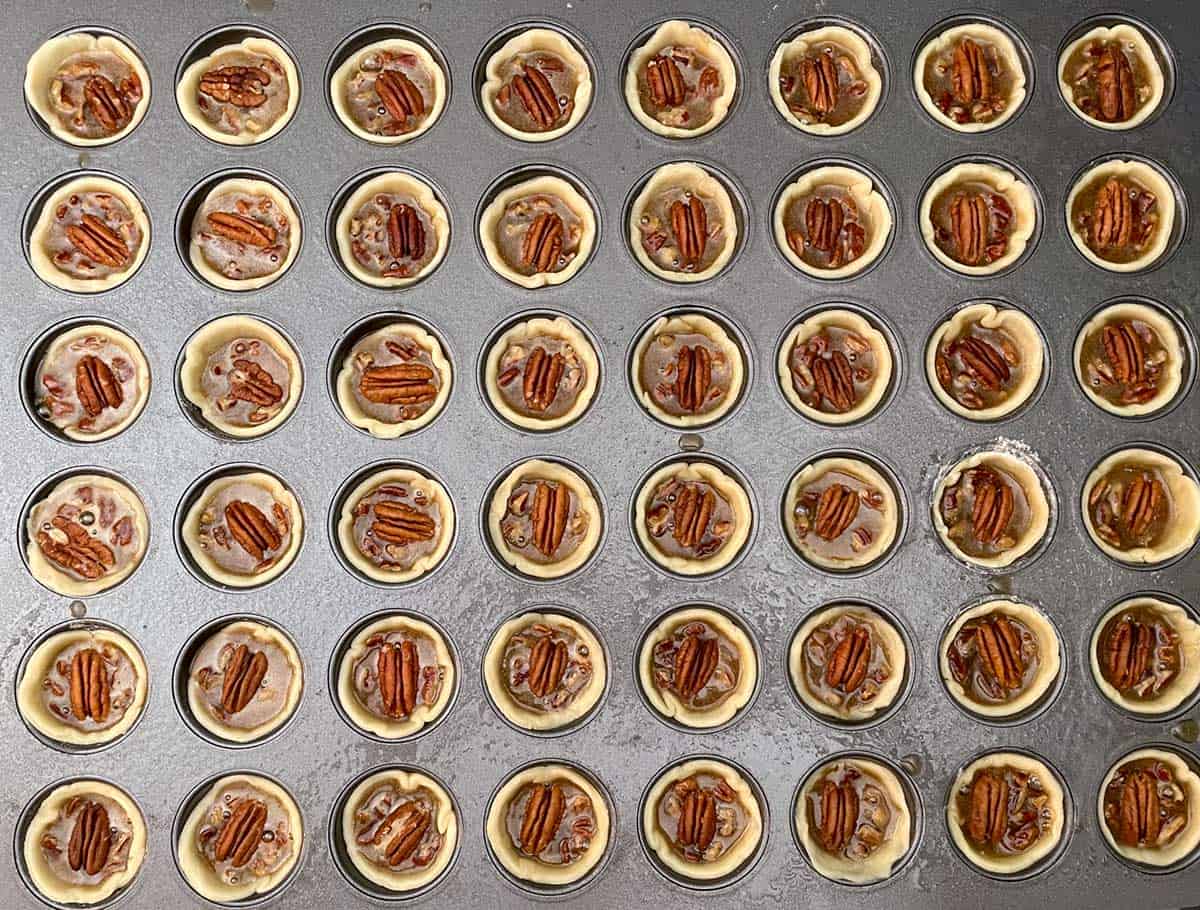 Cookie cups shaped into each cup mold with pecans and filling ready for the oven.