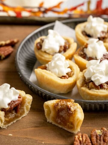 Pecan Pie Cookie cups with whip cream on top and one cut in half to show the inside of the cookie.