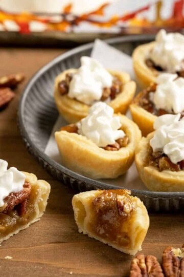 Pecan Pie Cookie cups with whip cream on top and one cut in half to show the inside of the cookie.