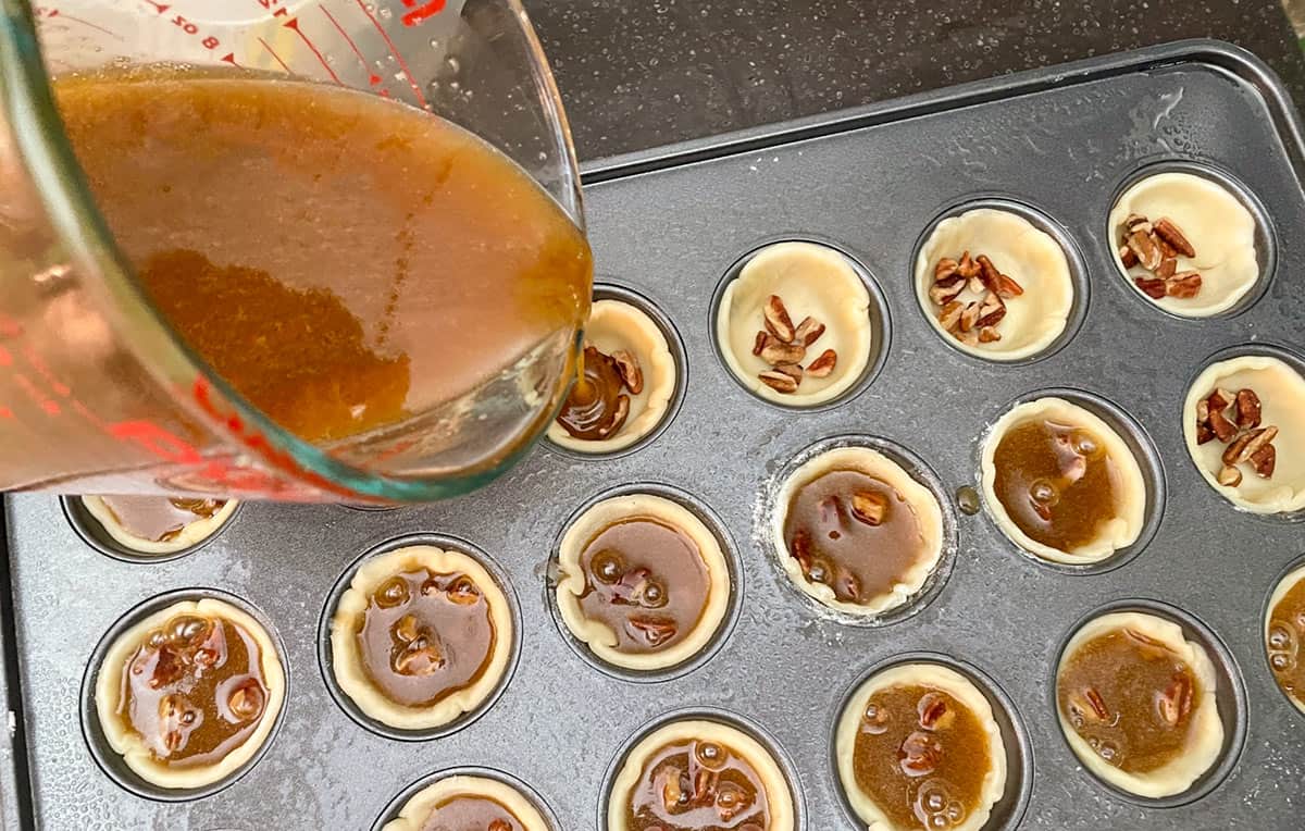 Cookie cups lined in pan with chopped pecans and pouring the filling into each cup.