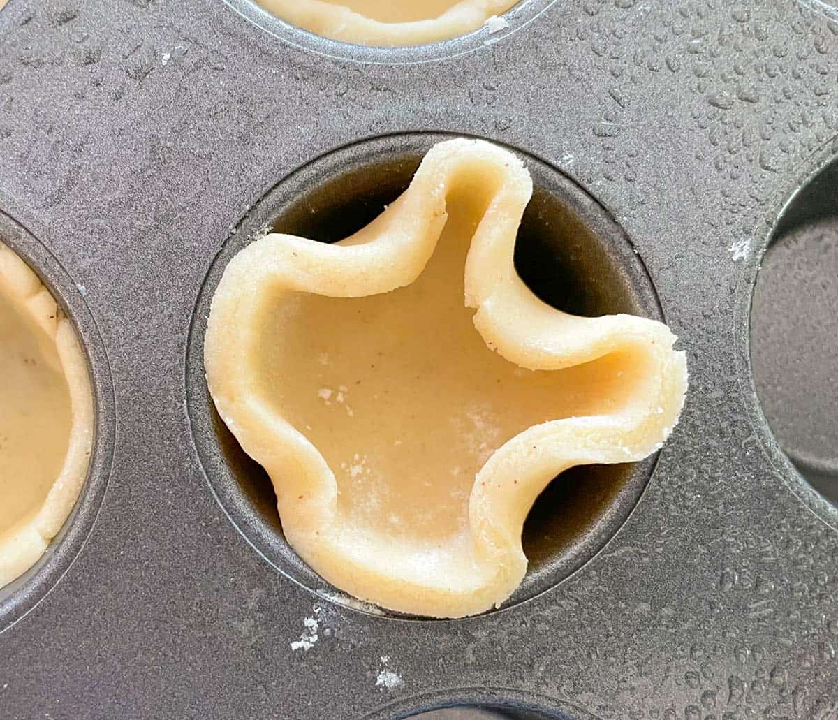 Adding a circle of cookie dough into a mini cup pan for cookie cups.