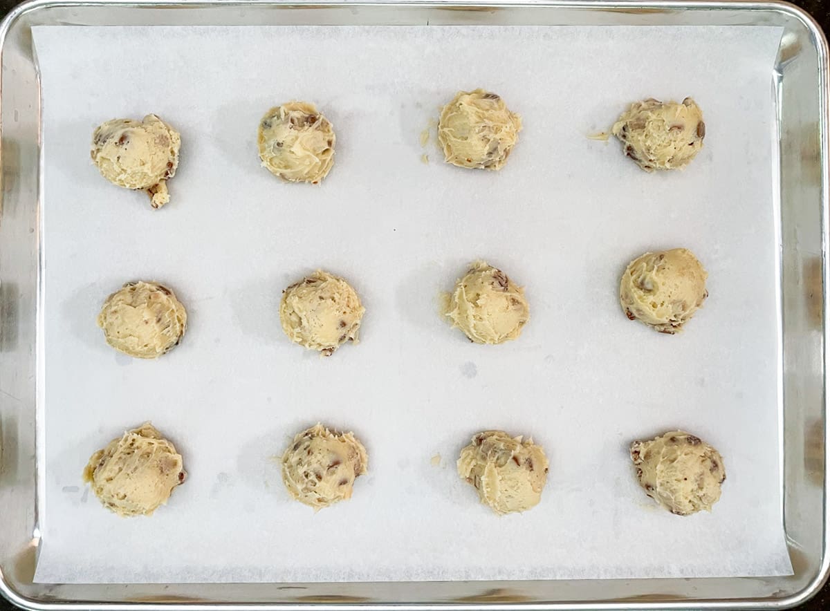 Twelve scoops of caramel and cinnamon with pecan cookies dough on a sheet pan.