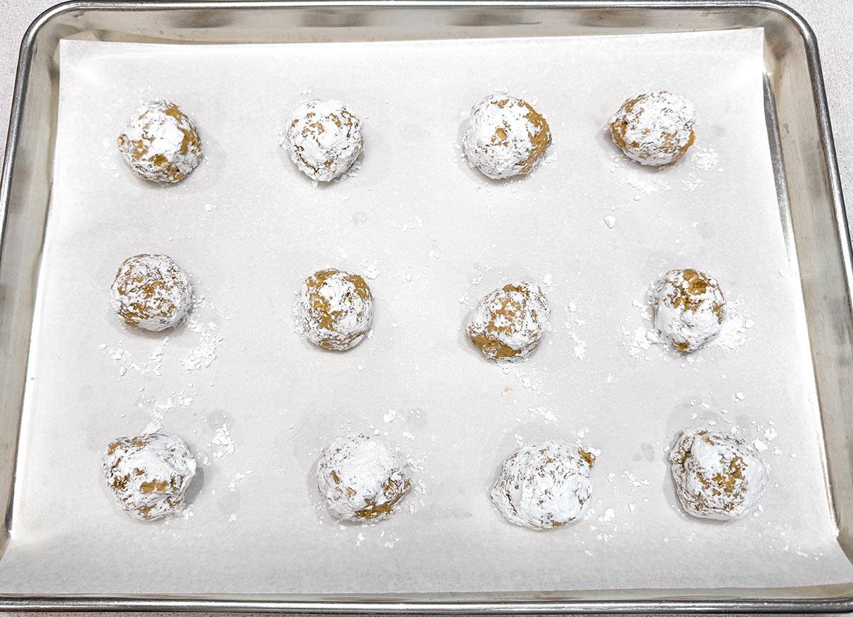 Coated cookie balls with powdered sugar on a sheet pan.
