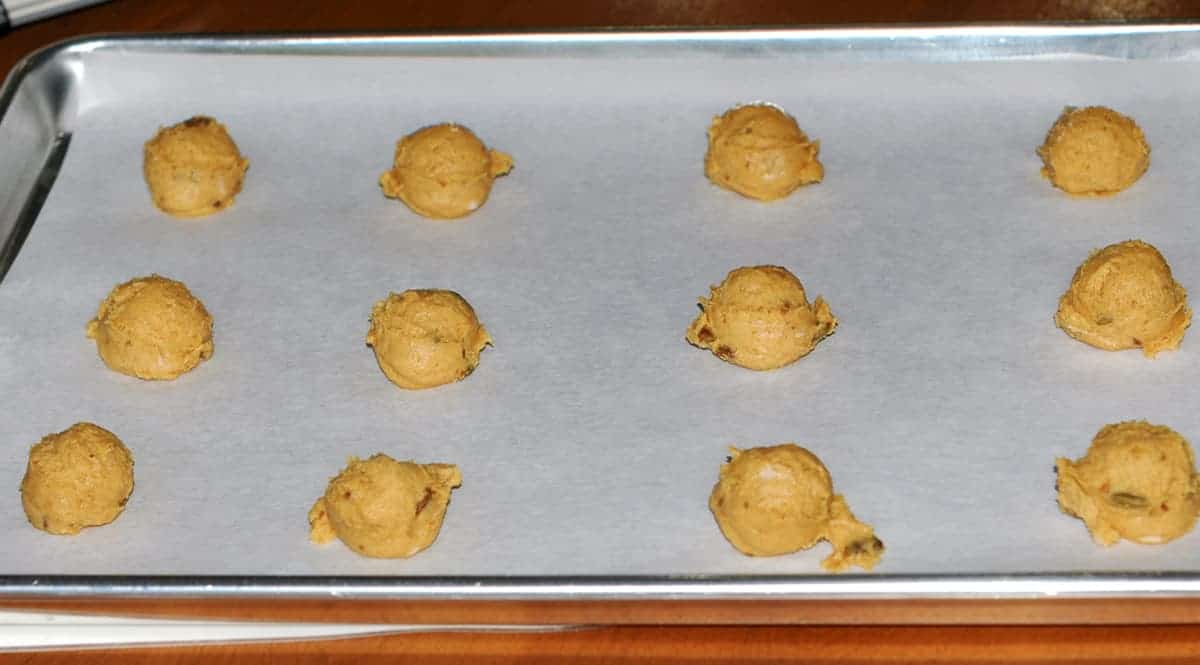 Pumpkin cookie dough scooped onto parchment-paper lined sheet pan.