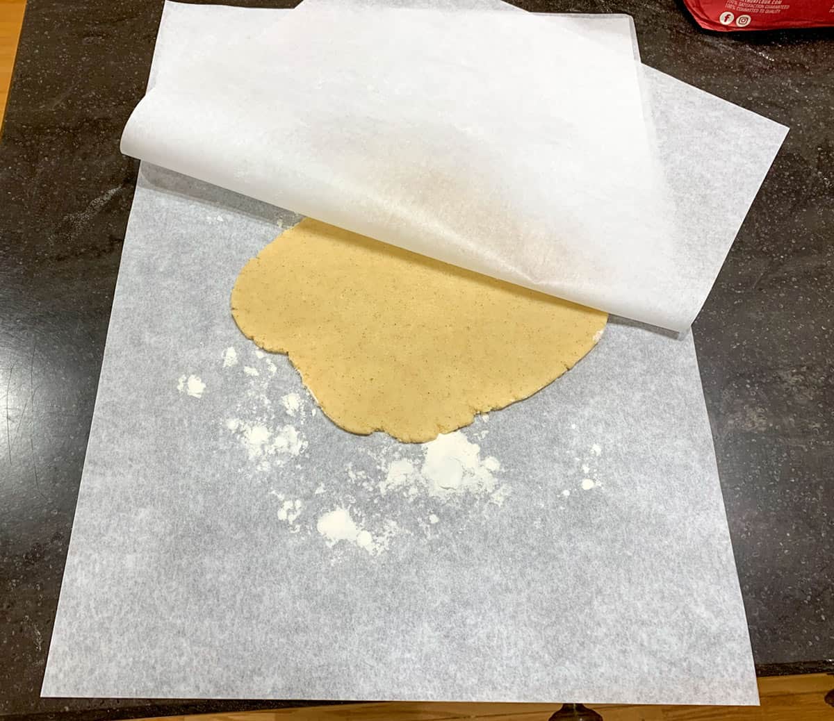 Lifting the top piece of parchment paper to show the rolled-out cookie dough.