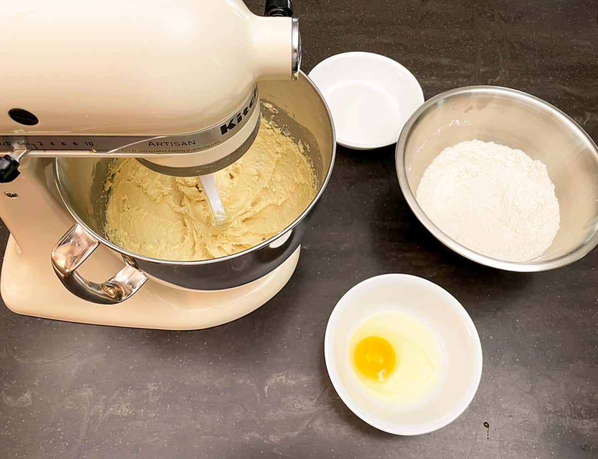 Butter and almond flour in the mixer with the rest of the ingredients of egg, flour mixture, and sugar ready to be added.