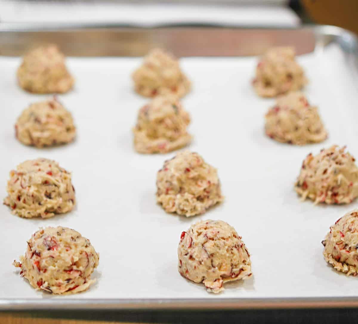 Cranberry and walnut cookie dough scooped onto parchment-paper lined sheet pan.