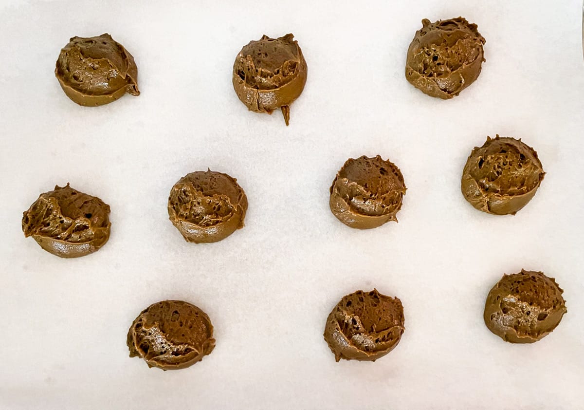 Ten molasses cookie mounds on a parchment-lined before baking.